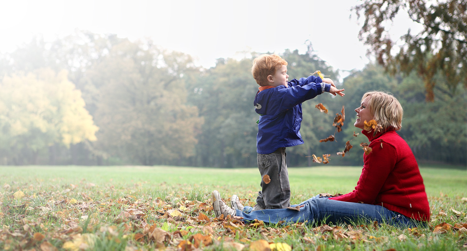 child playing in leaves with mother